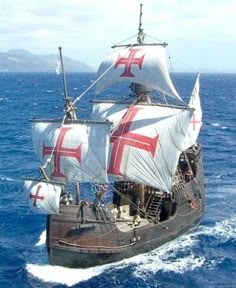 an old sailing ship in the ocean with a flag on it's mast and sails