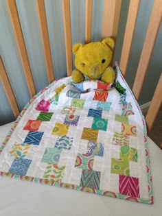 a yellow teddy bear sitting on top of a quilted blanket in a crib