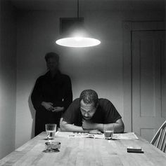 two men are standing behind a table with papers on it and one man is looking down