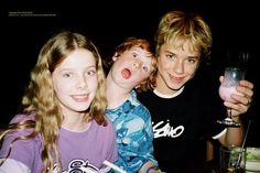 three young people posing for a photo with drinks in front of them and food on the table