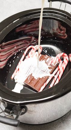 candy canes are being poured into a slow cooker with hot chocolate and marshmallows