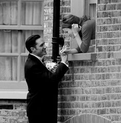 a man in a suit and tie standing next to a woman on a window sill