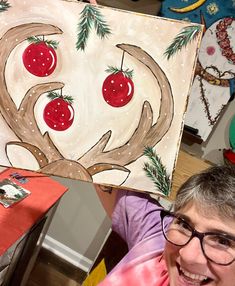 a woman holding up a painting with cherries on it's face and antlers