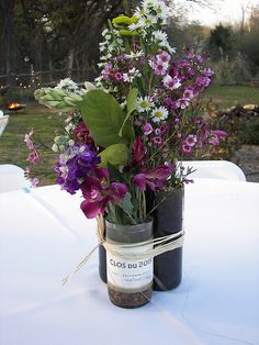 a vase filled with purple flowers sitting on top of a white tablecloth covered table