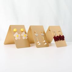 four different types of earrings are displayed in gold and red stands on a white surface