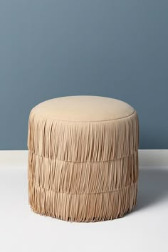 a round stool with fringed fabric on it in front of a blue wall and white floor