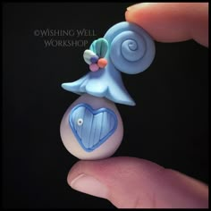 a hand holding a blue and white brooch with a heart on it's back