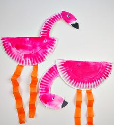 two pink flamingos made out of paper plates on a white surface with orange strips