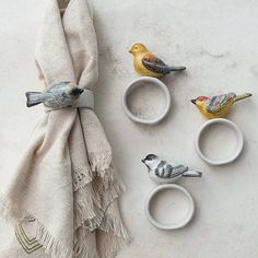 three small birds are sitting on napkins next to two cups with rings in them