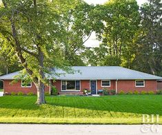 a red brick house sitting in the middle of a lush green field next to trees