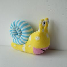 a yellow snail with blue and white stripes on it's back, sitting against a wall