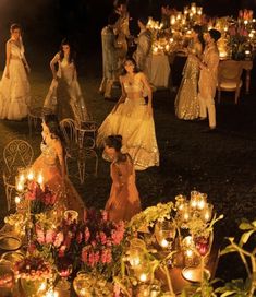 a group of women dressed in evening gowns sitting around a table with candles on it