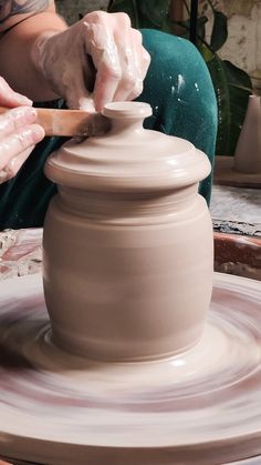 a woman is making a vase out of clay on a potter's wheel with her hands