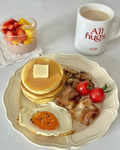 pancakes, bacon, and eggs on a plate next to a cup of coffee with strawberries