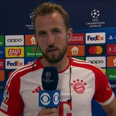 a man in a red and white shirt holding a microphone while standing next to a wall