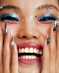 a woman with blue and silver makeup holding her hands to her face while smiling at the camera