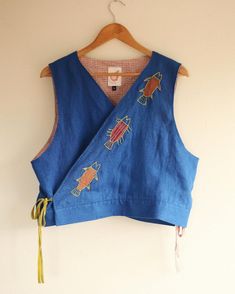 a women's blue top with embroidered animals on the front and back, hanging from a hanger