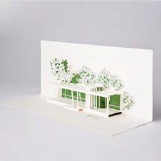 a white greeting card with a house and trees on the outside, in front of a gray background