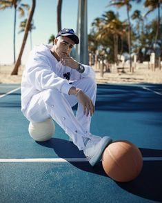 a young man sitting on top of a basketball court next to a basket ball in front of palm trees