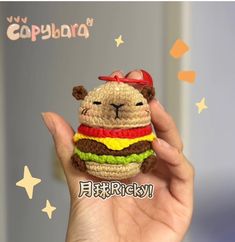 a hand holding a small crocheted stuffed animal with a hamburger on it's face