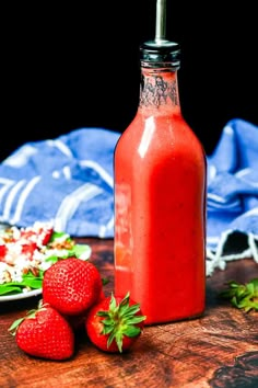 two strawberries sit next to a bottle of strawberry juice on a table with other fruit