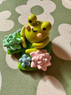 a frog figurine sitting on top of a green plate with flowers around it