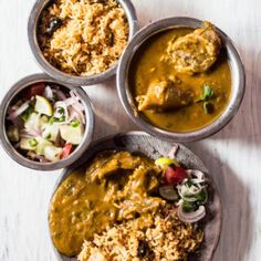 three metal bowls filled with food on top of a white wooden table next to other dishes