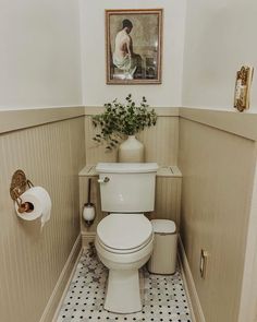 a white toilet sitting in a bathroom next to a painting on the wall and a potted plant