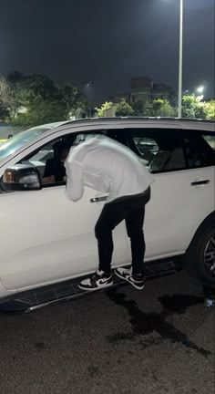 a man riding a skateboard on the side of a white car in a parking lot