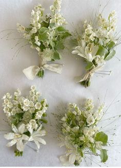 four bouquets of white flowers and greenery laid out on a sheet of paper