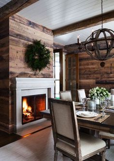 a dining room table with chairs and a fire place in the fireplace behind it, surrounded by wood paneling