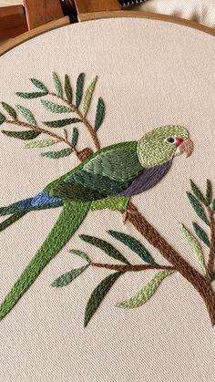 a green parrot sitting on top of a tree branch next to a white wall hanging