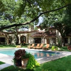 a large pool in front of a house with lawn chairs around it and trees surrounding the pool