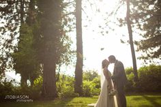 a bride and groom kissing in front of the sun shining through the trees on their wedding day