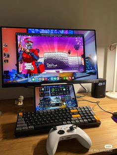 a computer monitor and keyboard sitting on top of a wooden desk next to a game controller