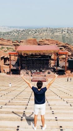 a man standing in front of an empty stage with his hands up to the sky