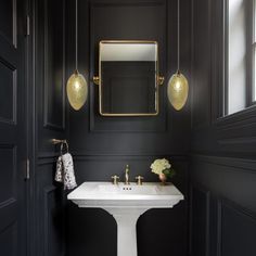 a white pedestal sink sitting under a mirror in a bathroom next to a black wall