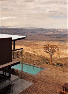 a wooden deck with chairs and a table next to a swimming pool in the desert