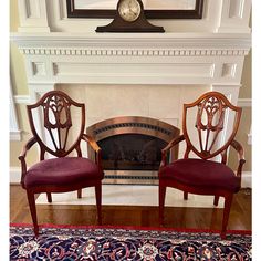 two chairs sitting next to each other in front of a fire place with a clock on the wall