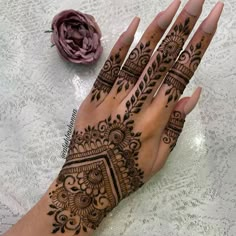 a woman's hand with henna tattoos on it and a flower in the background