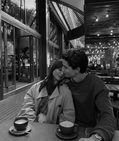 a man and woman sitting at a table in front of a coffee shop with their faces close to each other