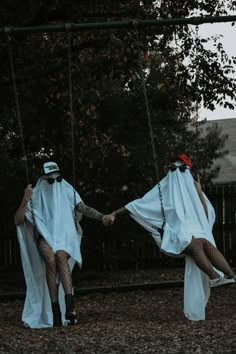 two people in white robes holding hands on a swing