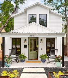 a small white house with two rocking chairs on the front porch and an open door