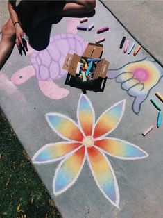 a woman is sitting on the sidewalk with chalk crayons in front of her