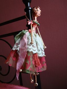 a doll is hanging from a black iron bed frame with pink and green fabric on it