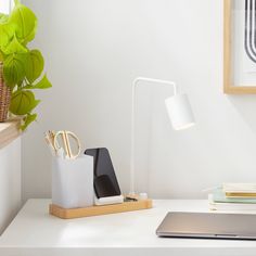 a white desk with a laptop, lamp and other items on it in front of a window