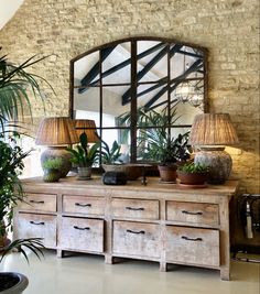 a large mirror sitting on top of a wooden dresser next to potted plants and lamps