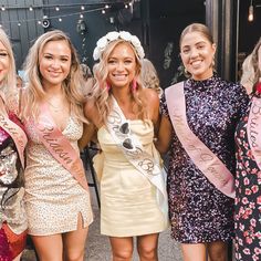 four beautiful young women standing next to each other wearing dresses and holding sashes in their hands