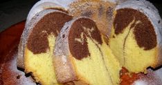 a bundt cake with chocolate and yellow frosting on a wooden platter covered in powdered sugar