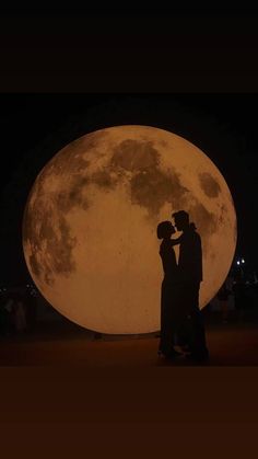 a man and woman standing in front of the full moon with their arms around each other